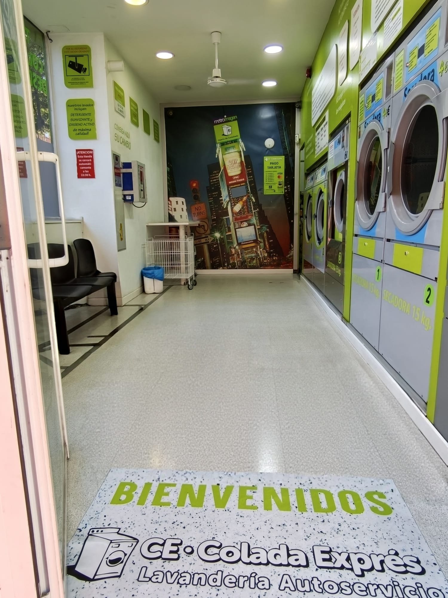 Entrada de Colada Exprés con la alfombra de bienvenida y la fila de lavadoras y secadoras
